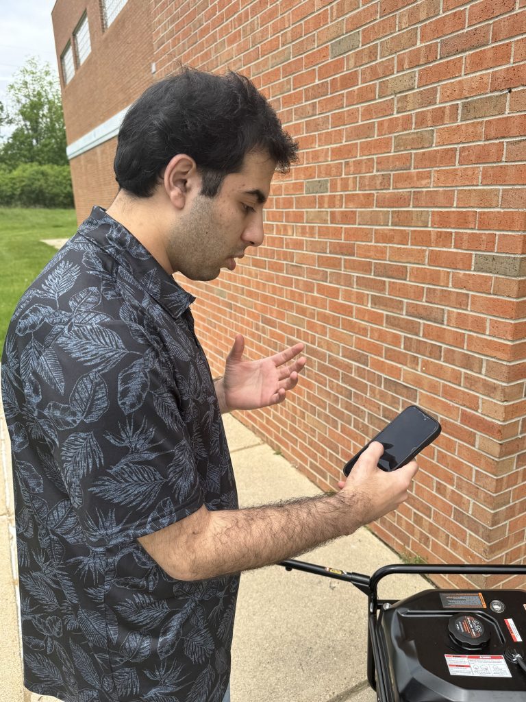 A graduate researcher using a phone during an acoustic diagnostic test on a portable generator